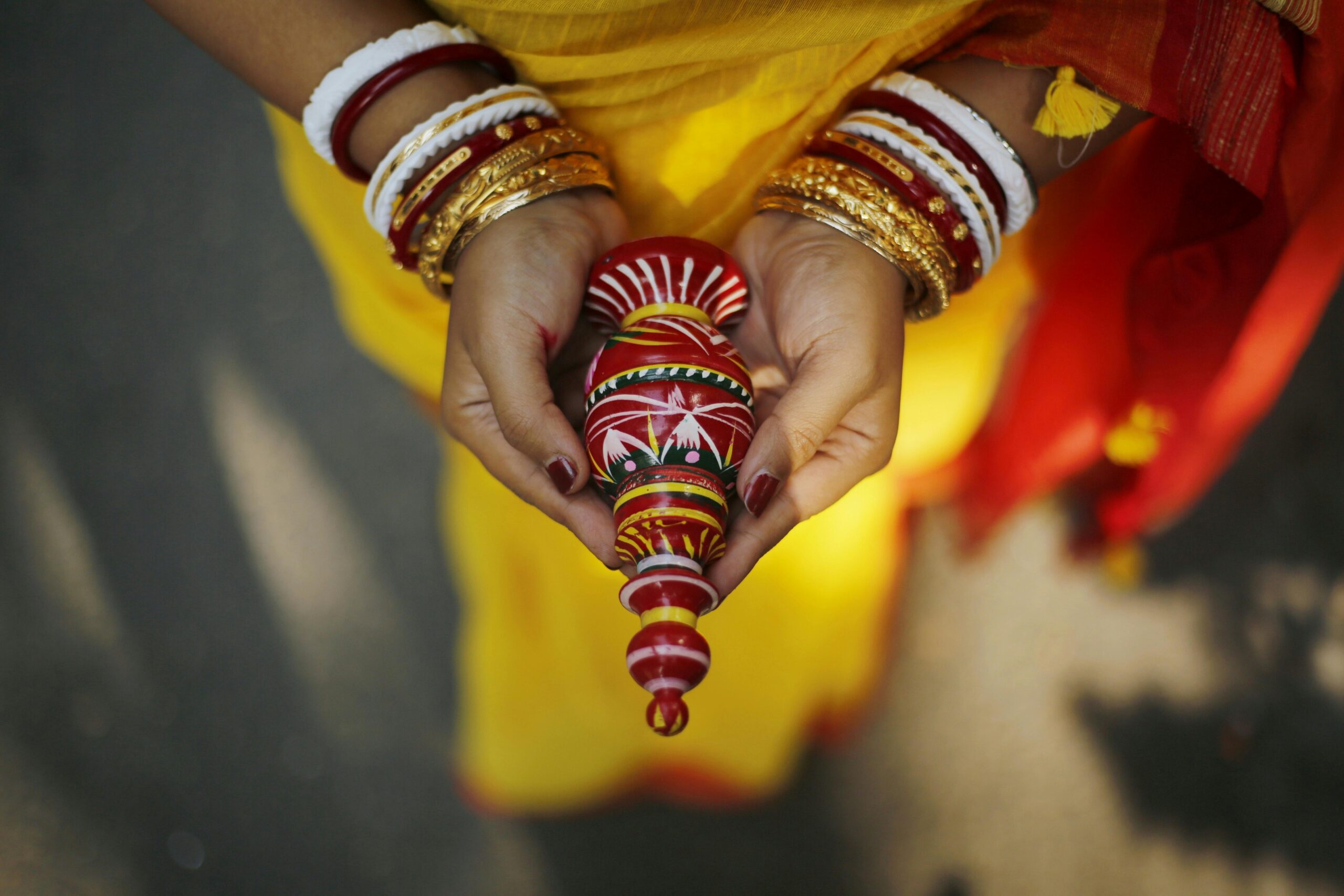 Close-up of a Bengali bride's hands holding a decorative conch shell during a traditional ceremony.